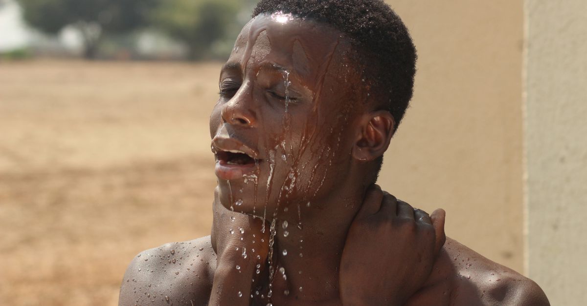 African American man enjoying a refreshing shower outdoors on a sunny day.