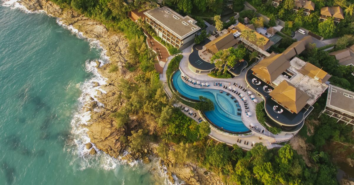 Stunning aerial view of a coastal resort featuring a luxurious infinity pool surrounded by lush greenery.