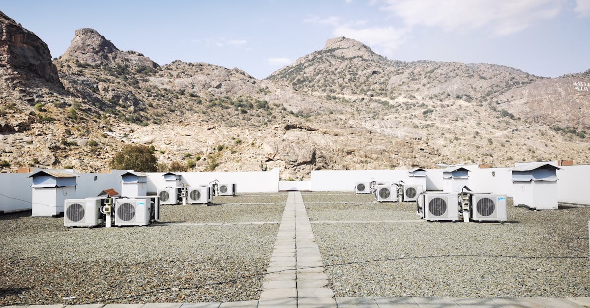 Rooftop air conditioning units on a gravel surface with a mountainous backdrop under a clear sky.