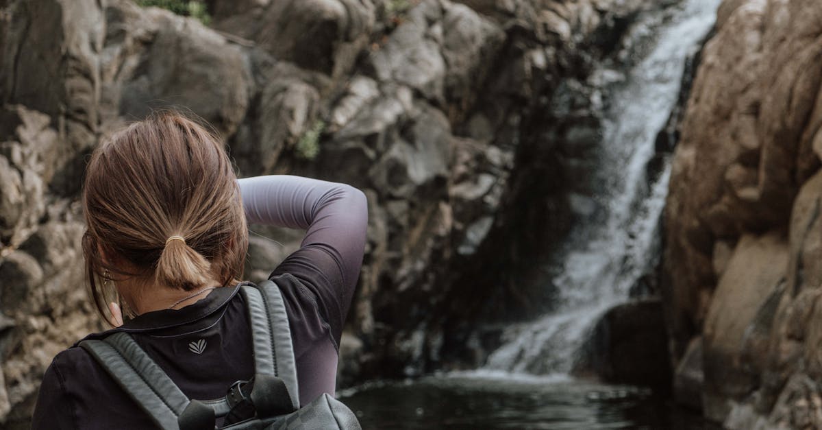 A backpacker stands before a serene waterfall in a rocky landscape, capturing the beauty of nature.