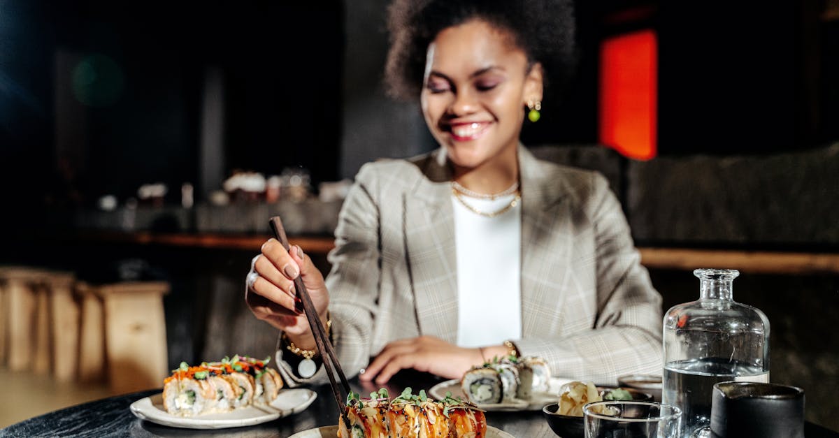 A smiling woman enjoys sushi with chopsticks at a cozy restaurant.
