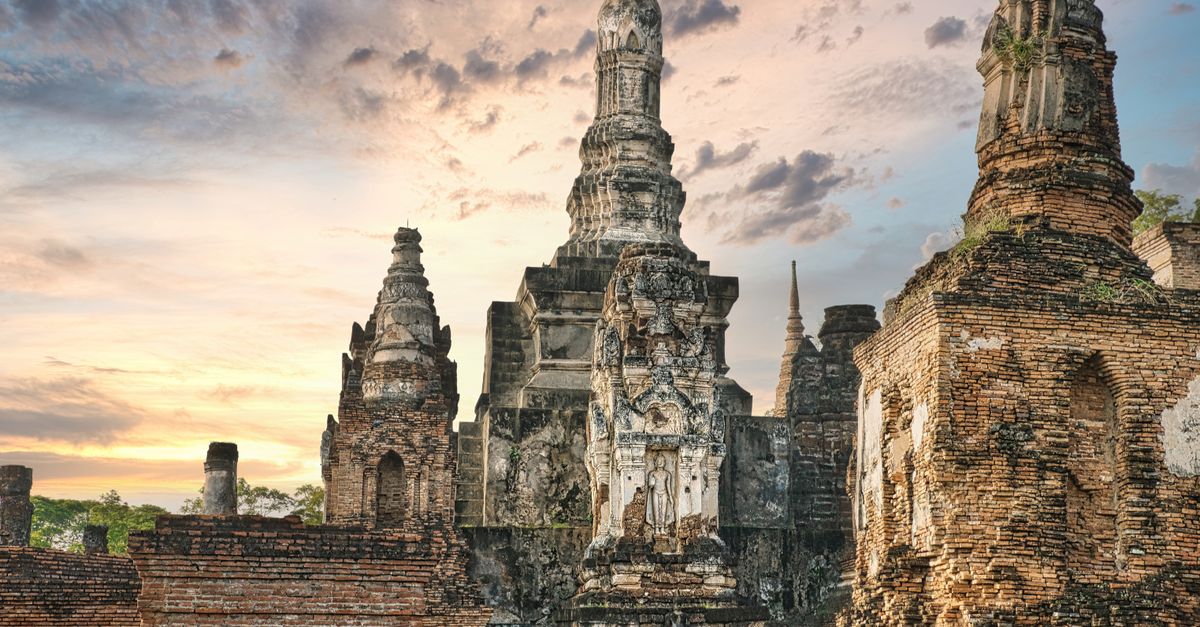 Ancient temple ruins of Wat Mahathat with a stunning sunset sky in Sukhothai, Thailand.