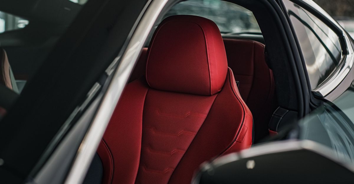 A close-up shot of a sleek car interior featuring a luxurious red leather seat illuminated by soft sunlight.