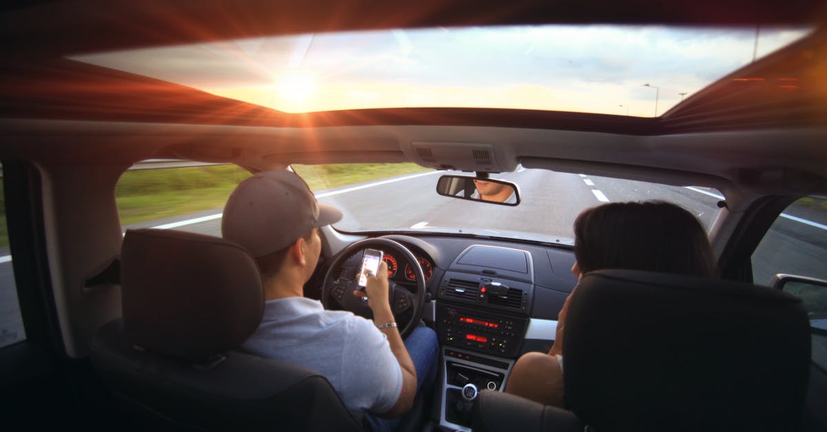 Driver using phone while driving at sunset with passenger in vehicle.