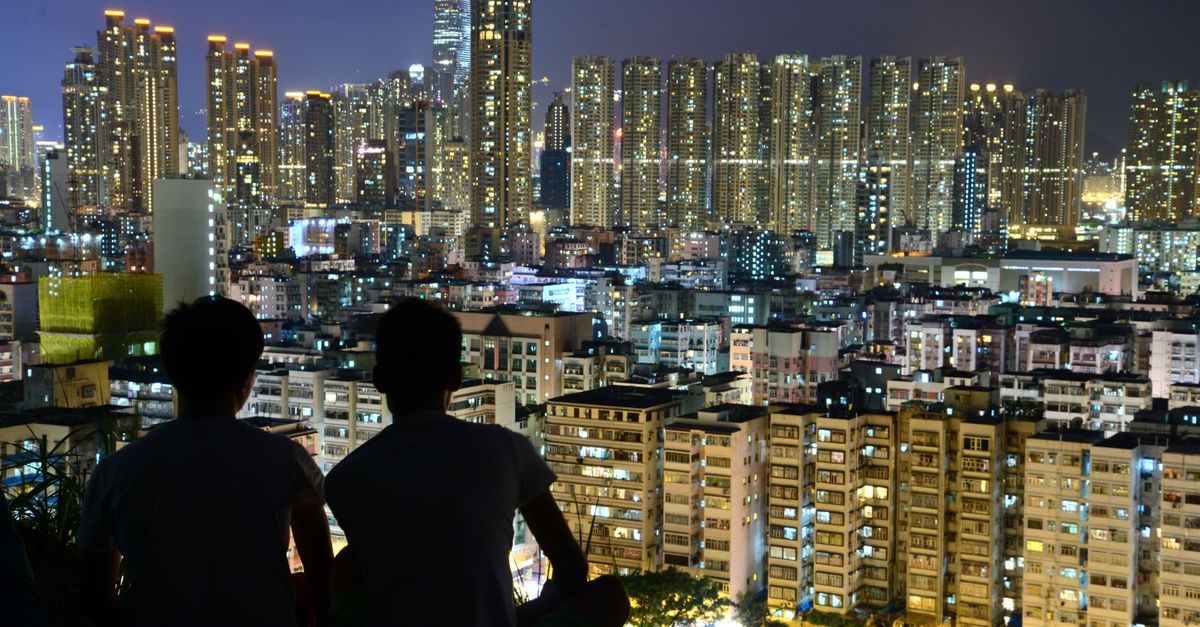 Two people silhouette overlooking illuminated city skyline at night, capturing urban beauty.